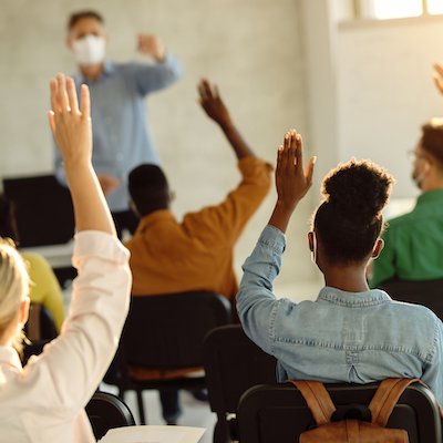 Students raising hands in a classroom - CREDIT Drazen Zigic Shutterstock